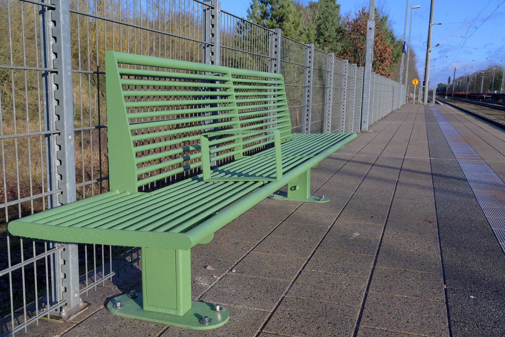 Grüne Sitzbank auf einem Bahnsteig.