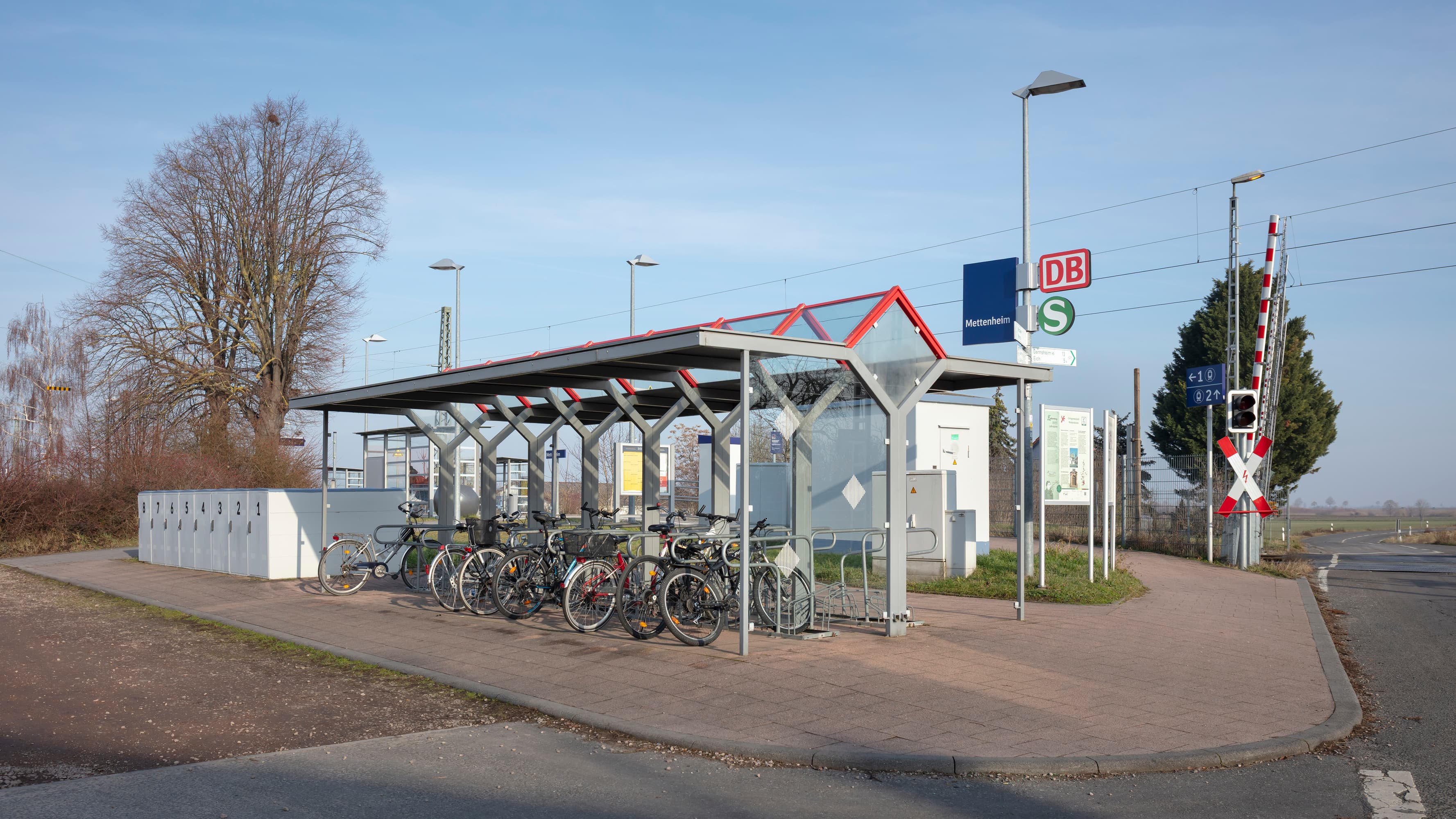 Eine überdachte Fahrradabstellanlage neben dem Bahnhofsschild, daneben sind die Fahrradboxen erkennbar.