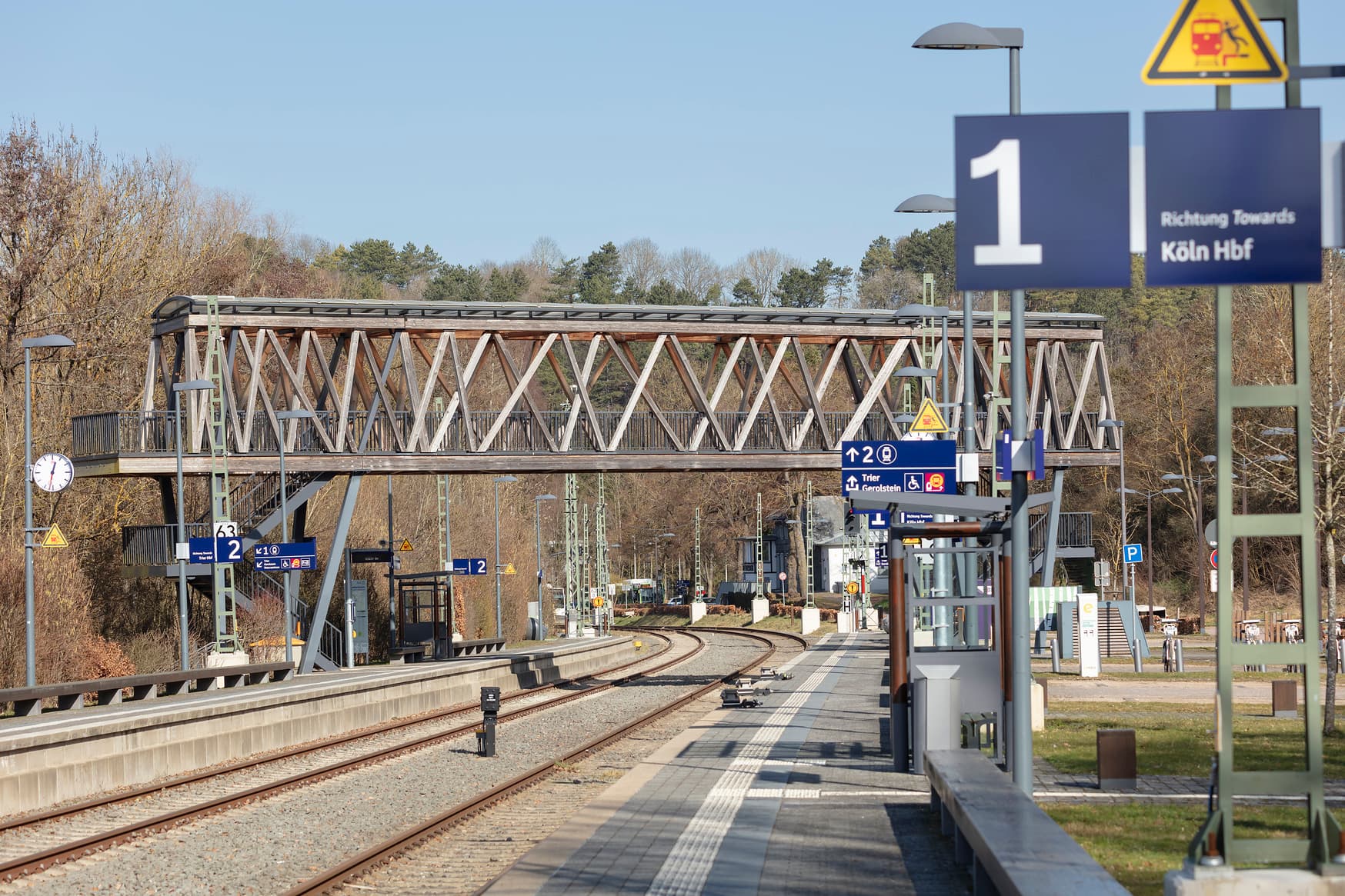 Blick auf die Gleise und Bahnsteige mit Sitzgelegenheiten, Wetterschutzhäuschen, neuer Beschilderung und taktilem Blindenleitstreifen.