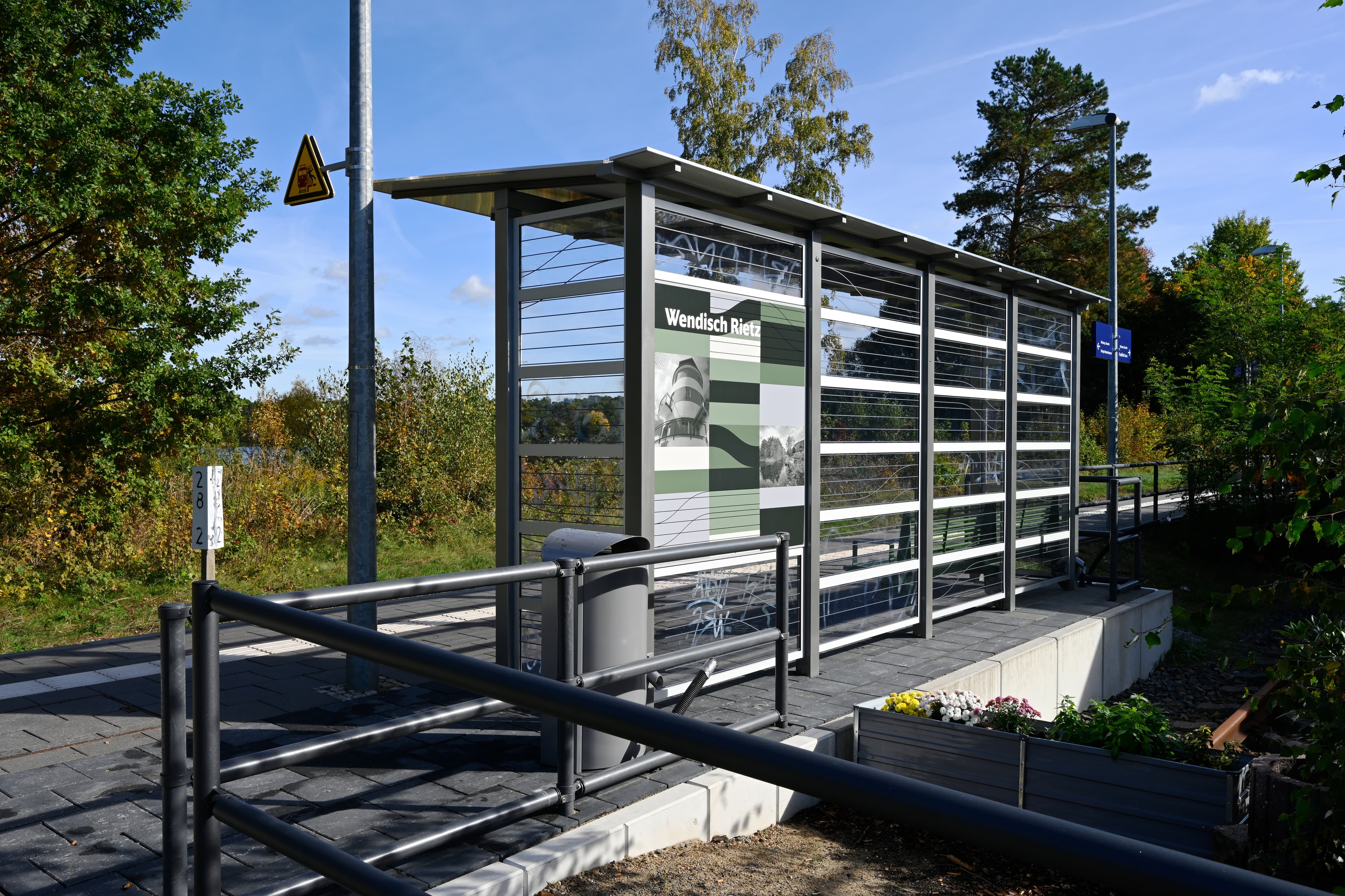 Ein Wetterschutzhaus neben einem Geländer auf einem Bahnsteig.