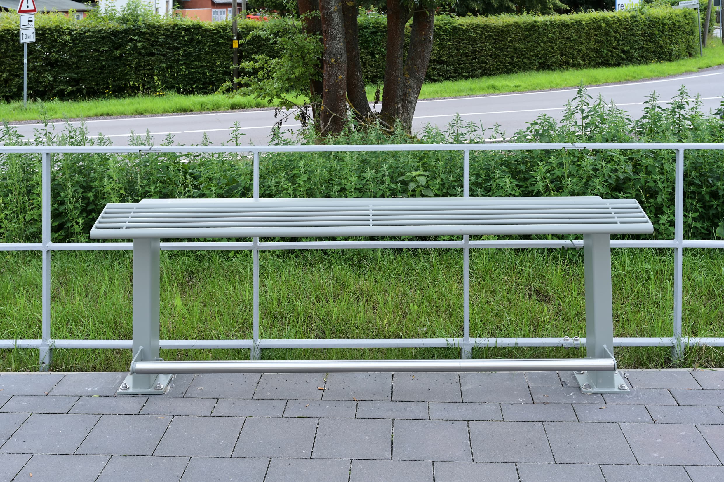 ein Anlehner mit grauem Rundrohrstahl im Eingangsbereich, Grünfläche im Hintergrund.