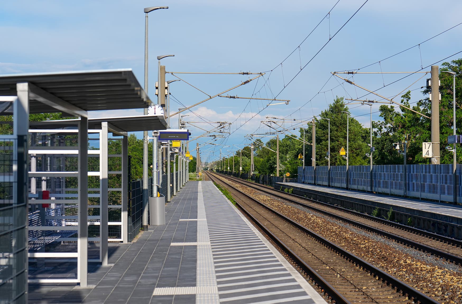 Zwei Bahnsteige mit Wetterschutzhäuschen, Reisendeninformation und taktilem Leitsystem auf dem Boden.