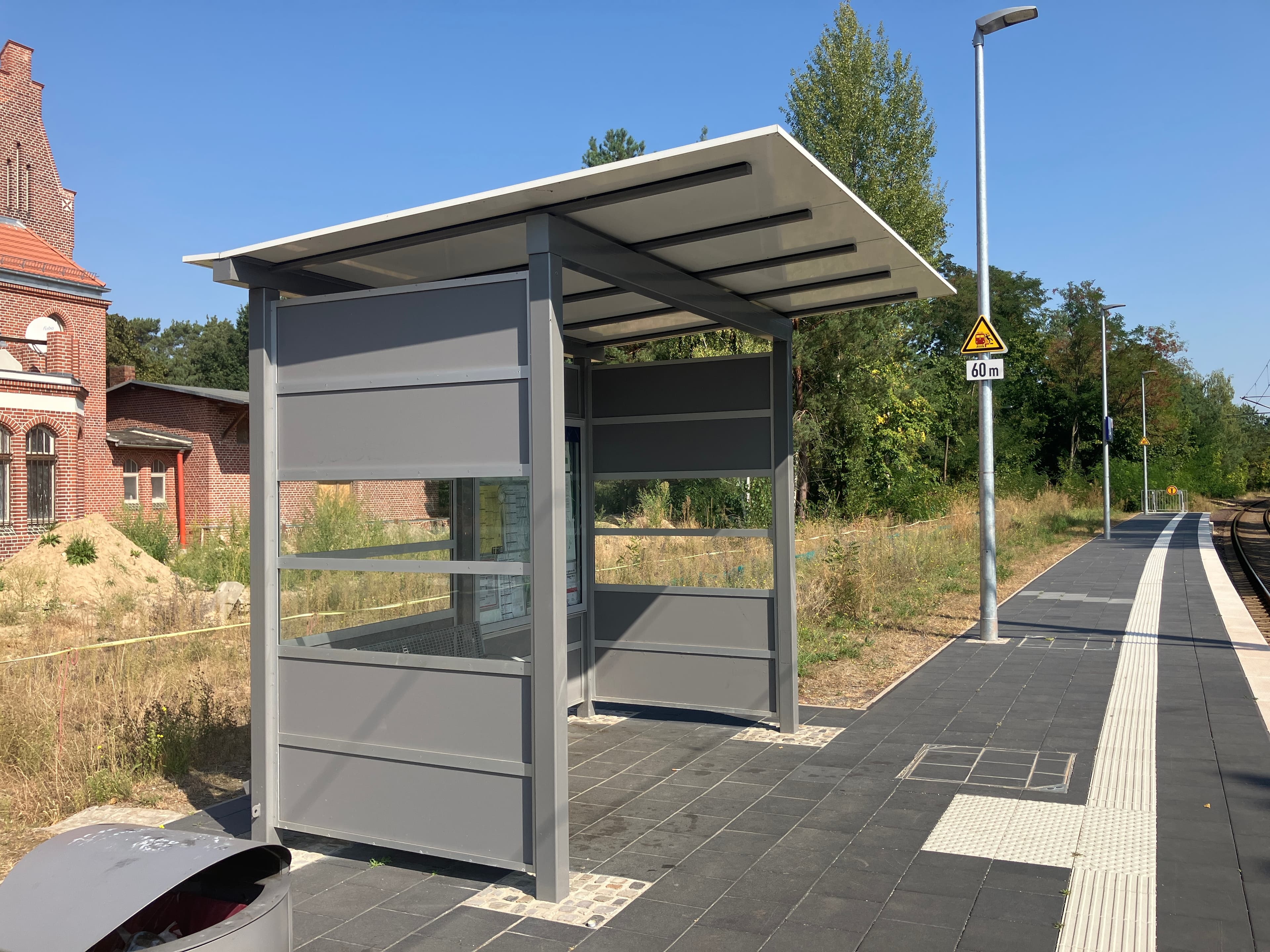 Blick auf ein graues Wetterschutzhäuschen an einem Bahnsteig.