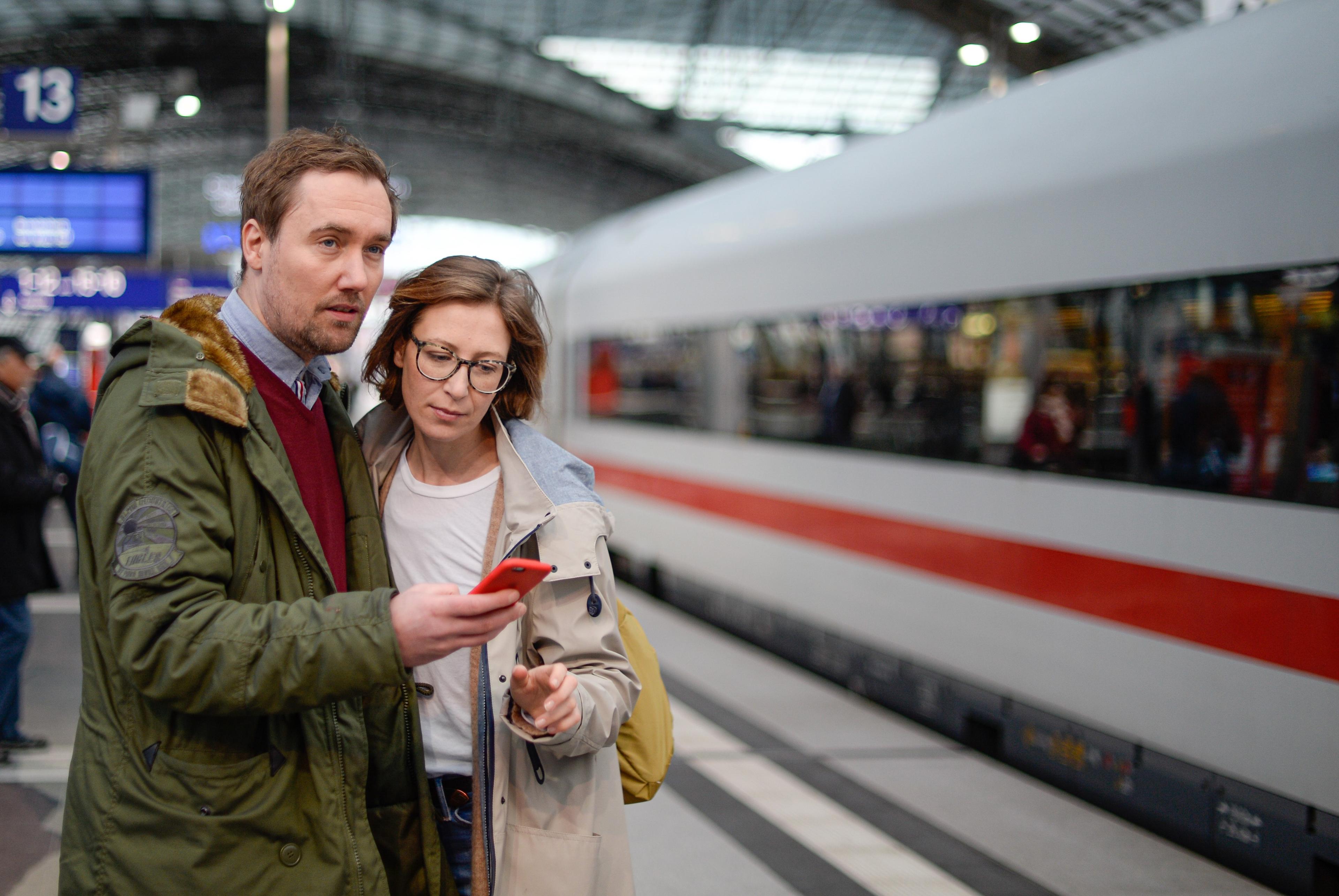 Travellers on the platform with a smartphone in their hand.