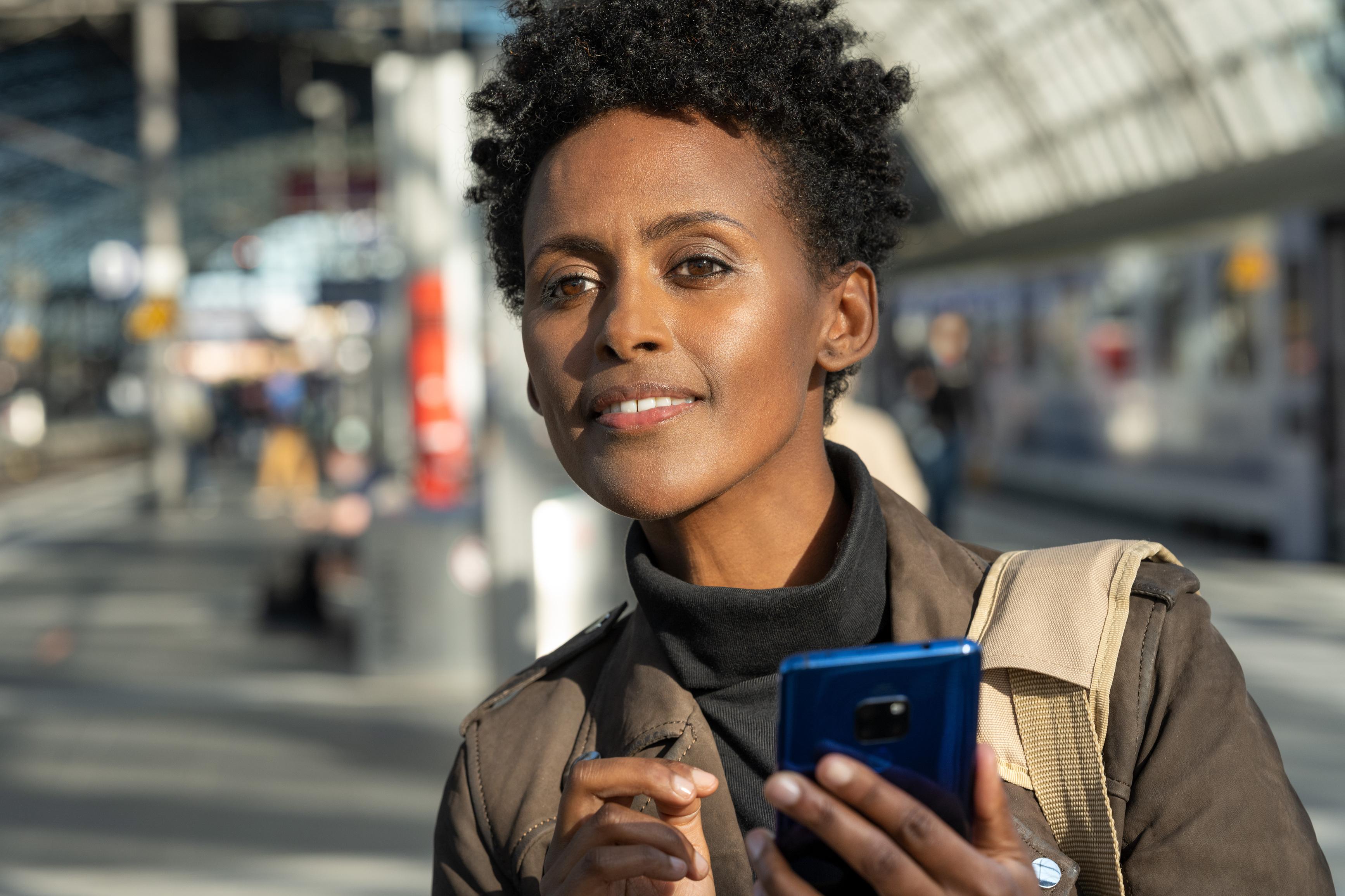 A young woman with a smartphone in her hand is standing on the platform at Berlin Hauptbahnhof.