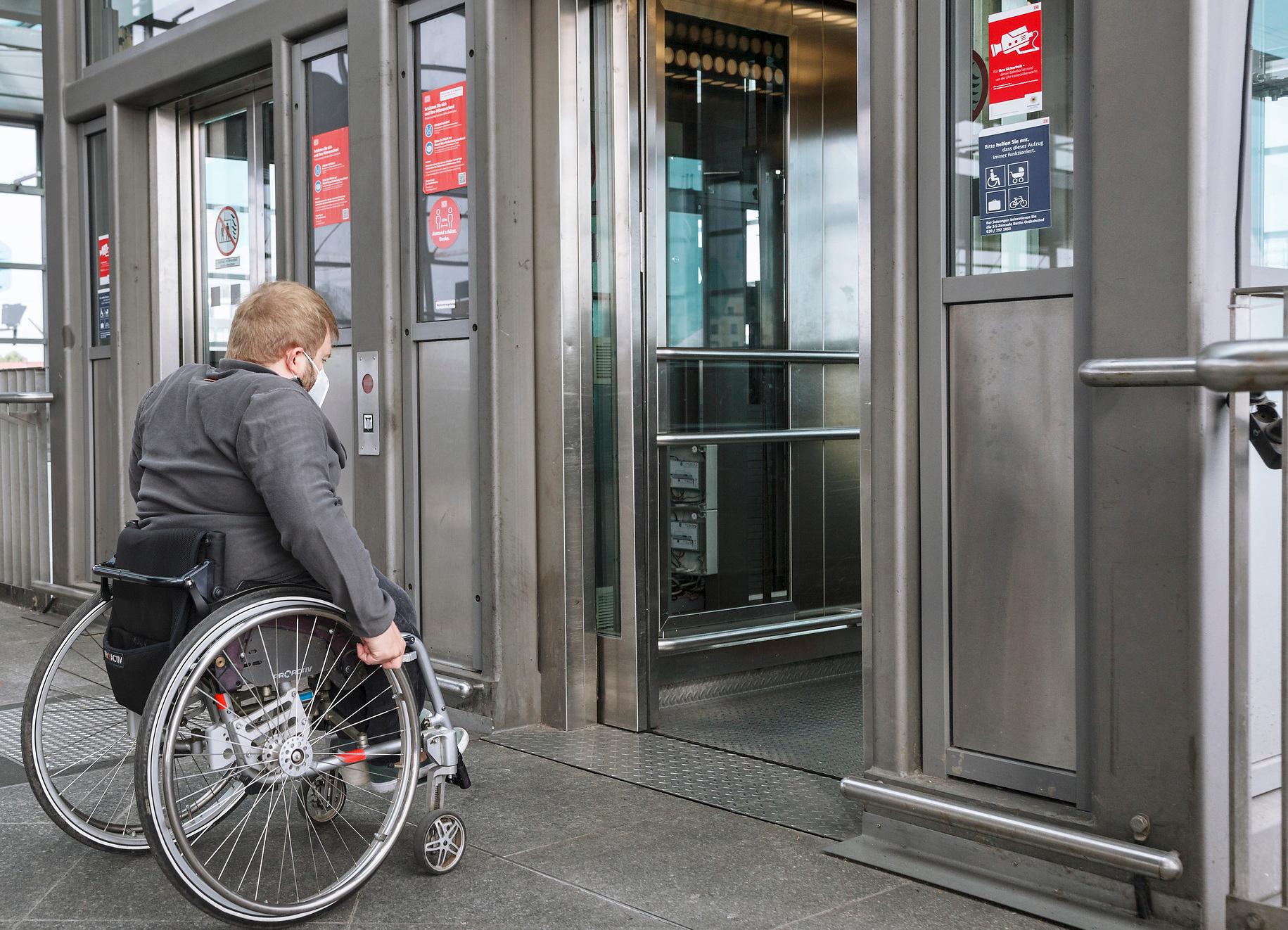 Ein Reisender in einem Rollstuhl nutzt einen Aufzug auf einem barrierefreien Bahnhofsgleis.