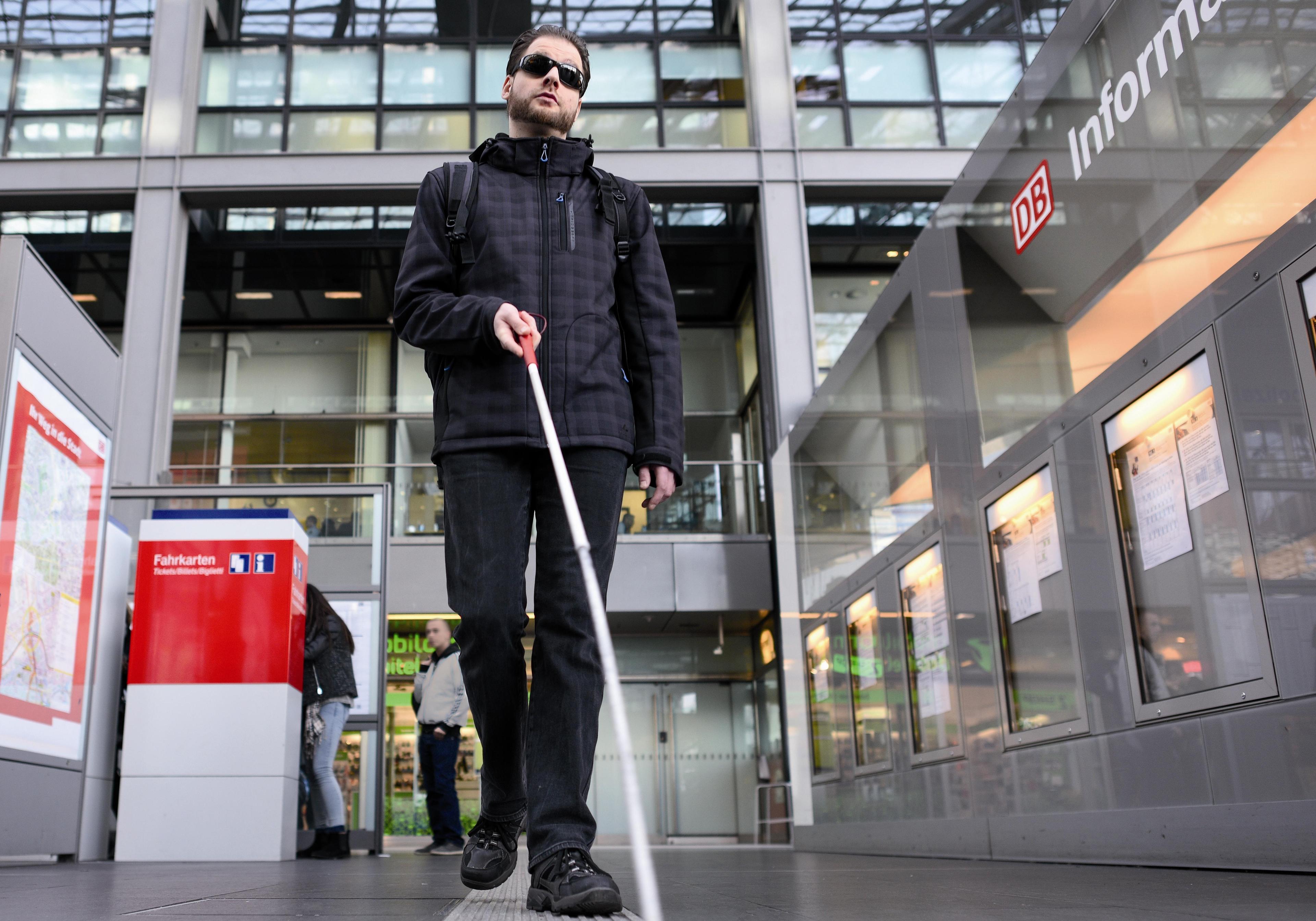 Visually impaired man with a long stick follows the tactile guidance system at Berlin Hauptbahnhof.