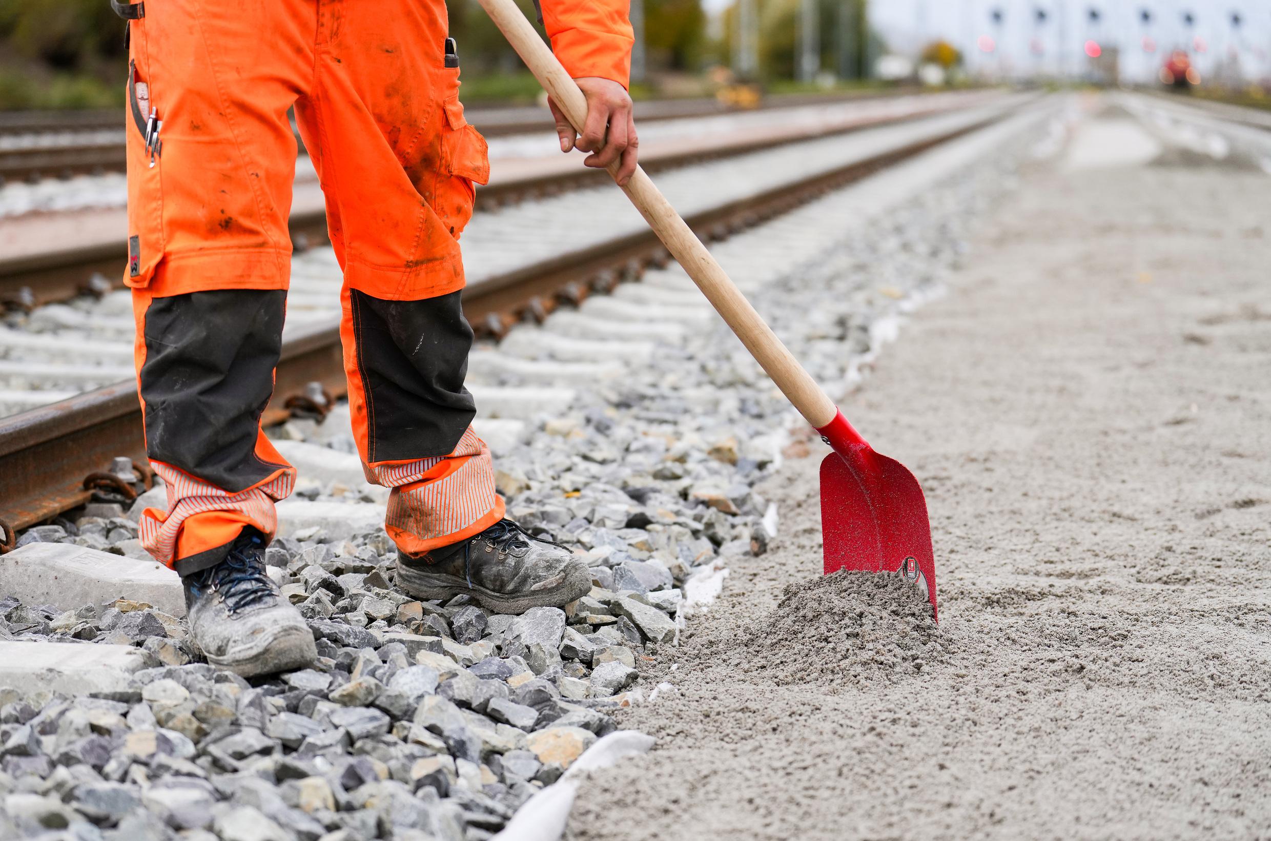 A construction worker works on the ground at a track bed with a shovel.